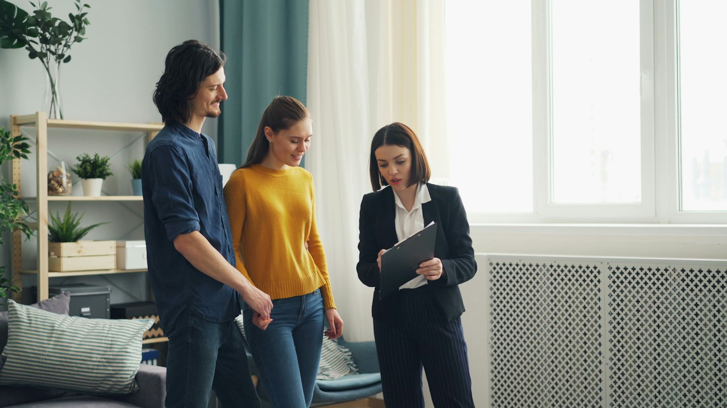 Immobilienmakler zeigt einem Paar in einer modernen Wohnung Dokumente.