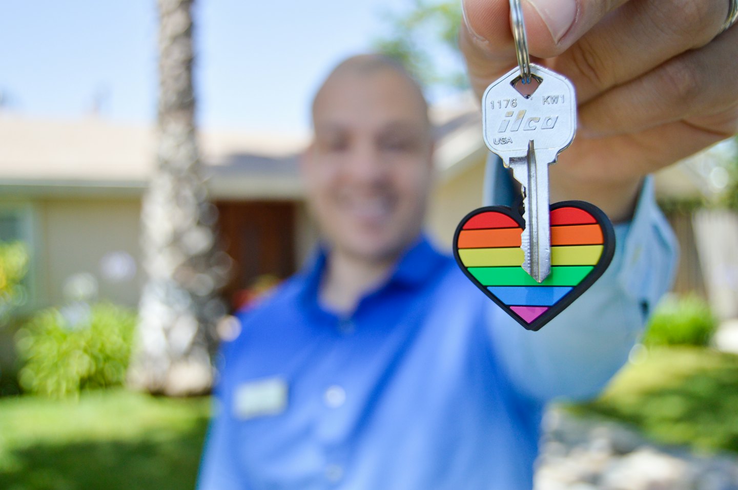 Person hält einen Hausschlüssel mit einem Regenbogen-Herz-Schlüsselanhänger.